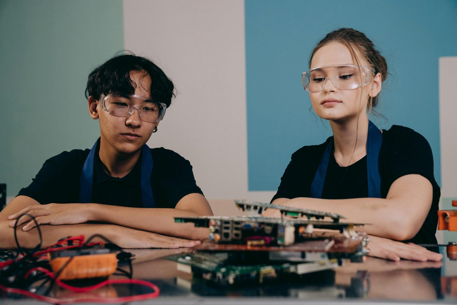 Two young engineers wearing safety goggles focus on an electronic project indoors.